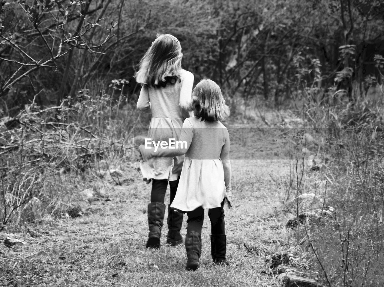 Rear view of girls walking on field against trees