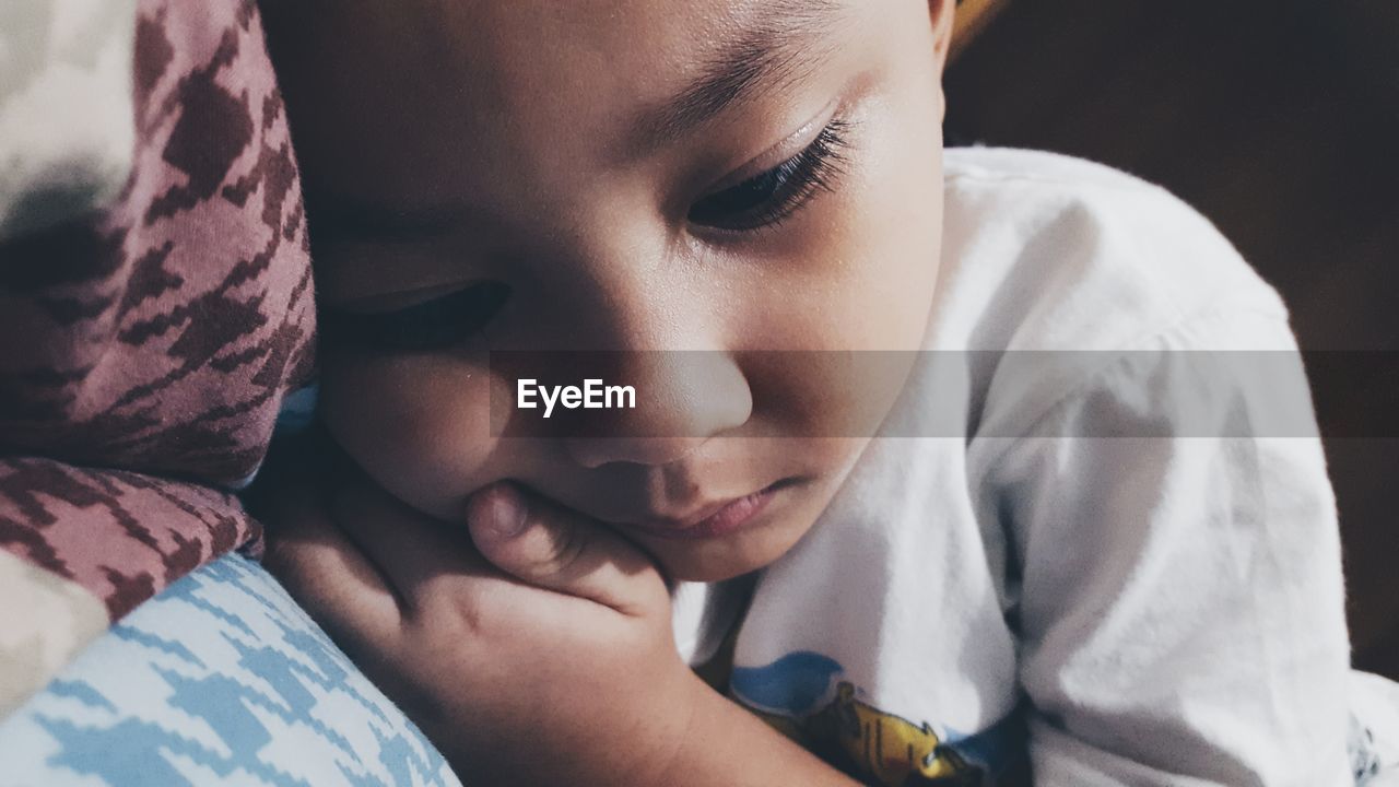 Close-up of sad boy lying on bed