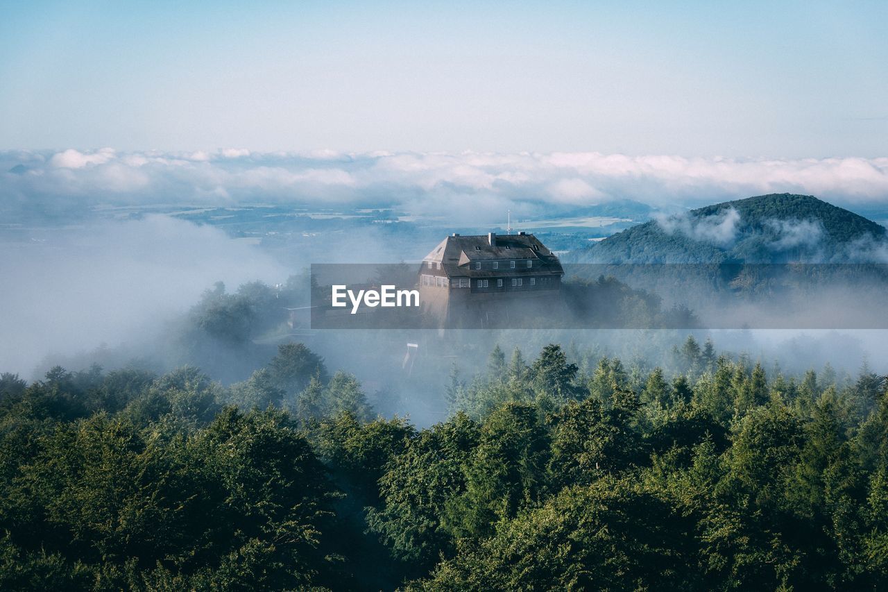 House surrounded by trees against sky during foggy weather