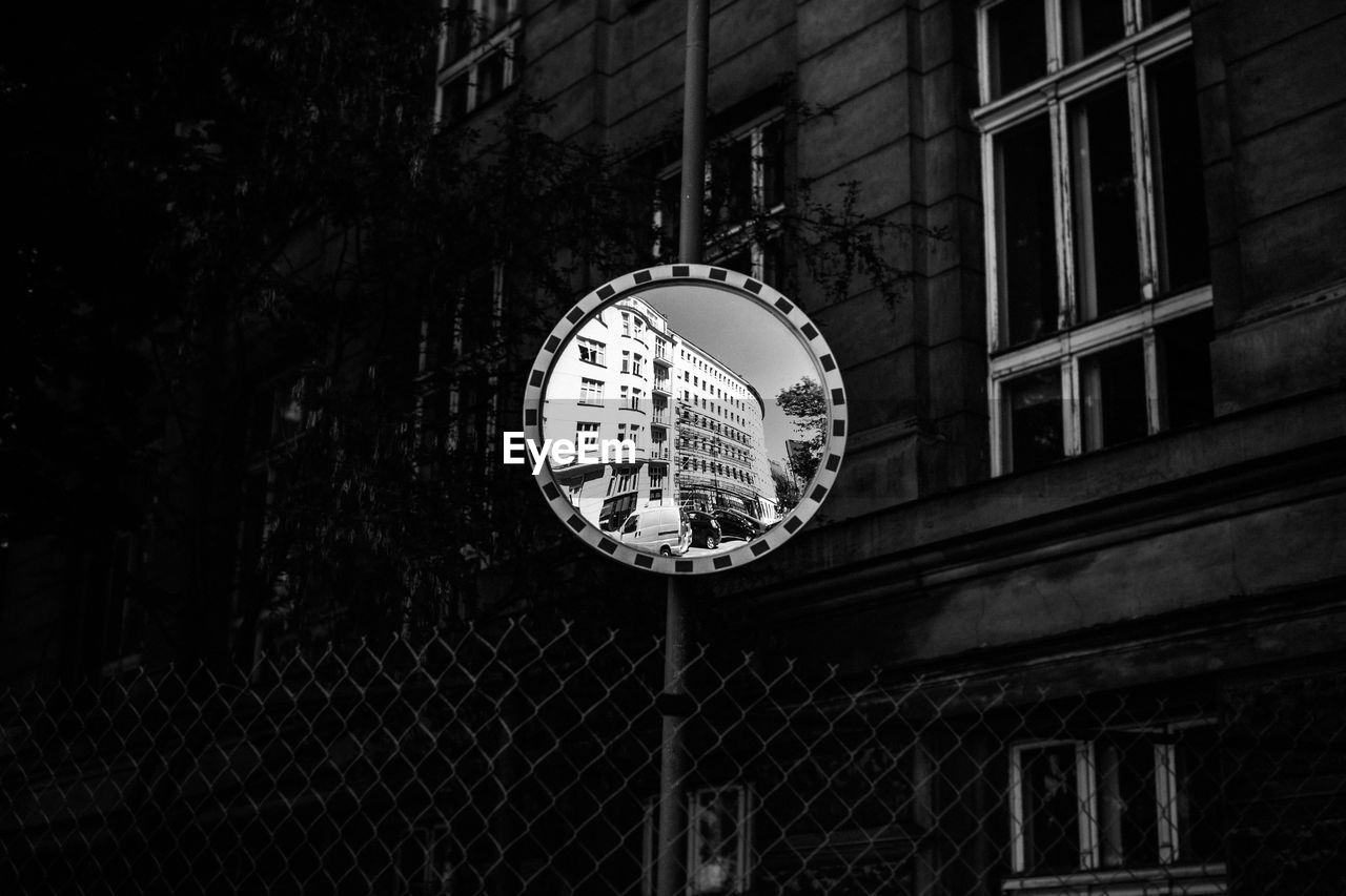 Low angle view of road mirror with reflection against building