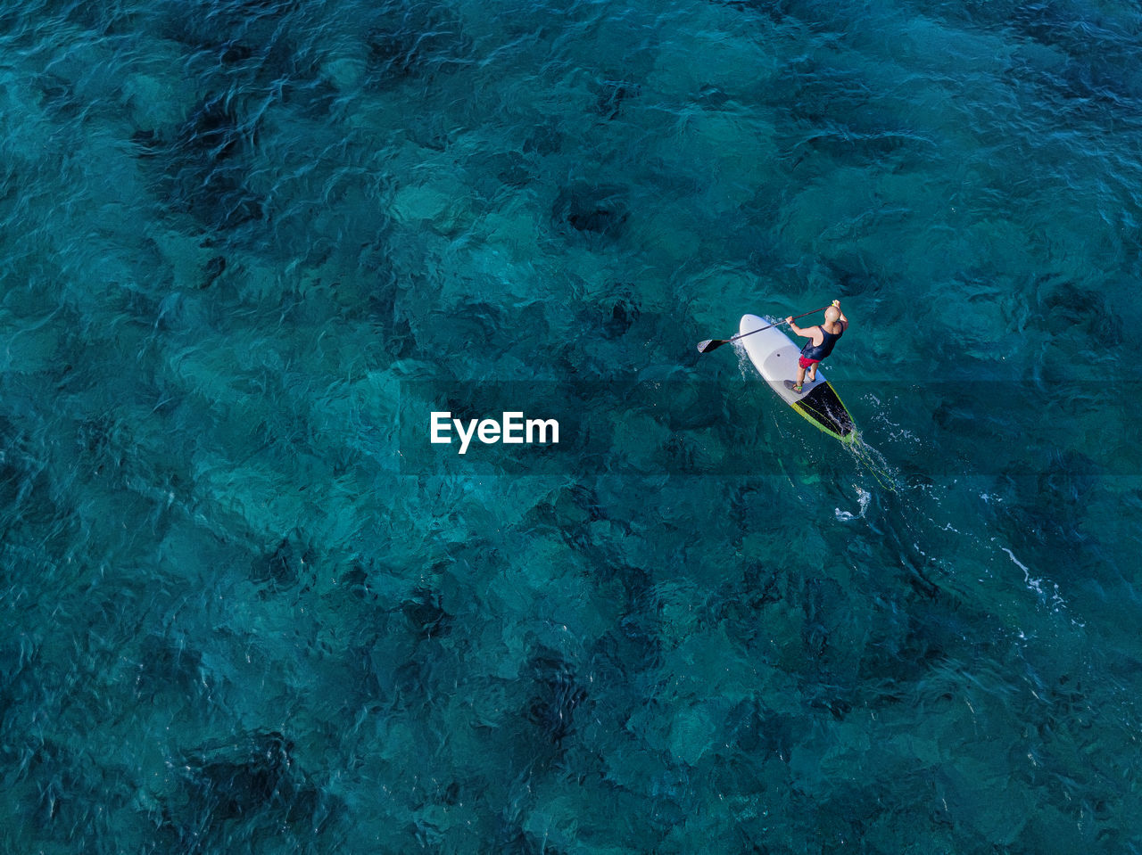 Aerial view of man paddleboarding in blue waters of north male atoll