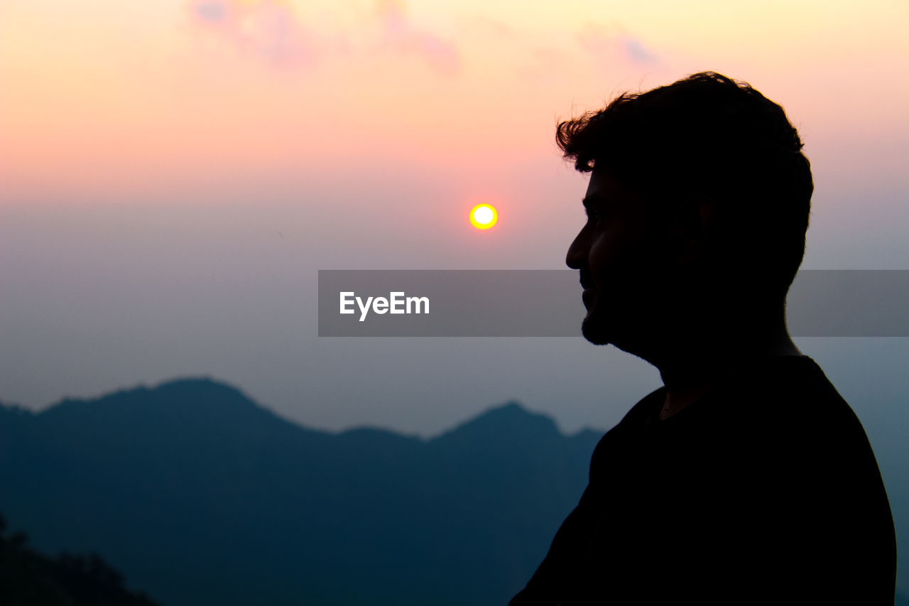 SIDE VIEW OF SILHOUETTE MAN AGAINST MOUNTAINS DURING SUNSET