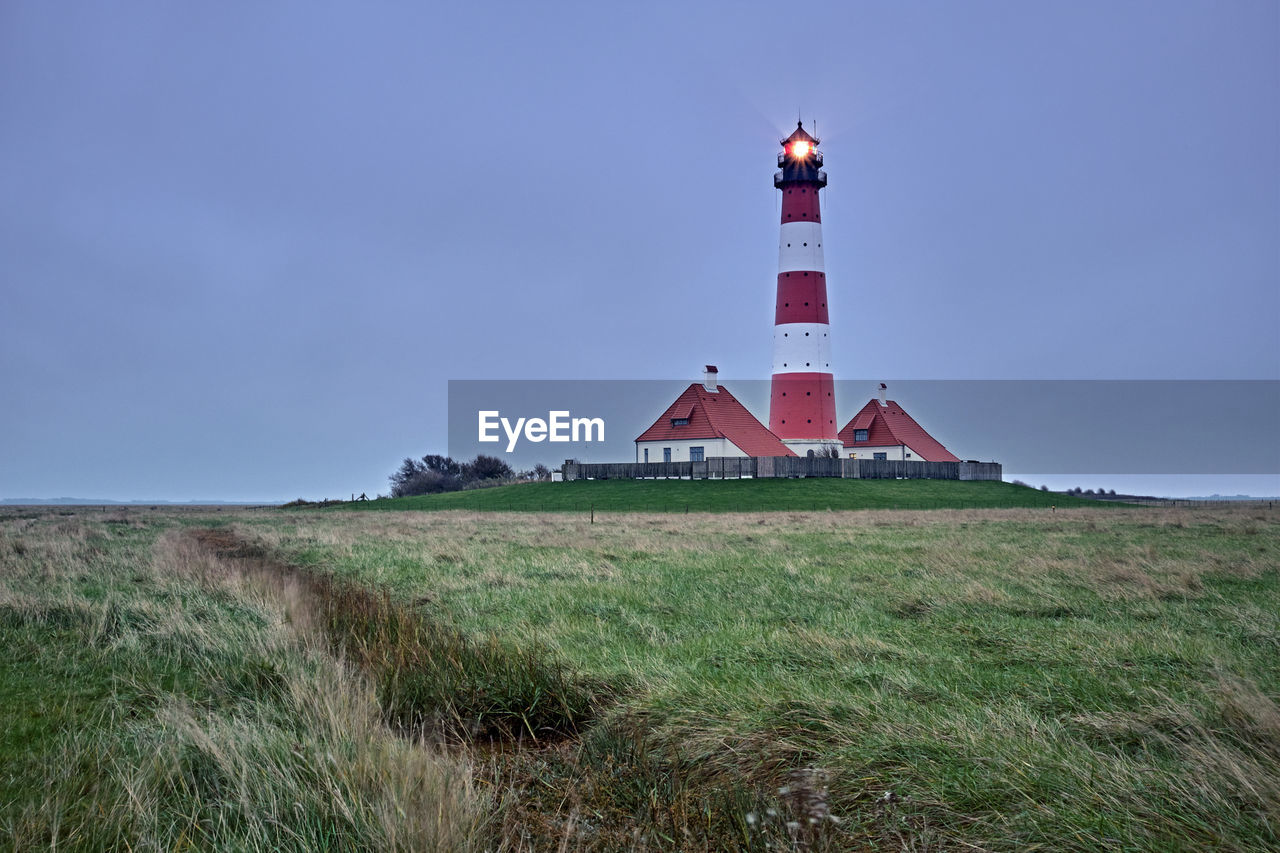 Lighthouse on field by building against sky