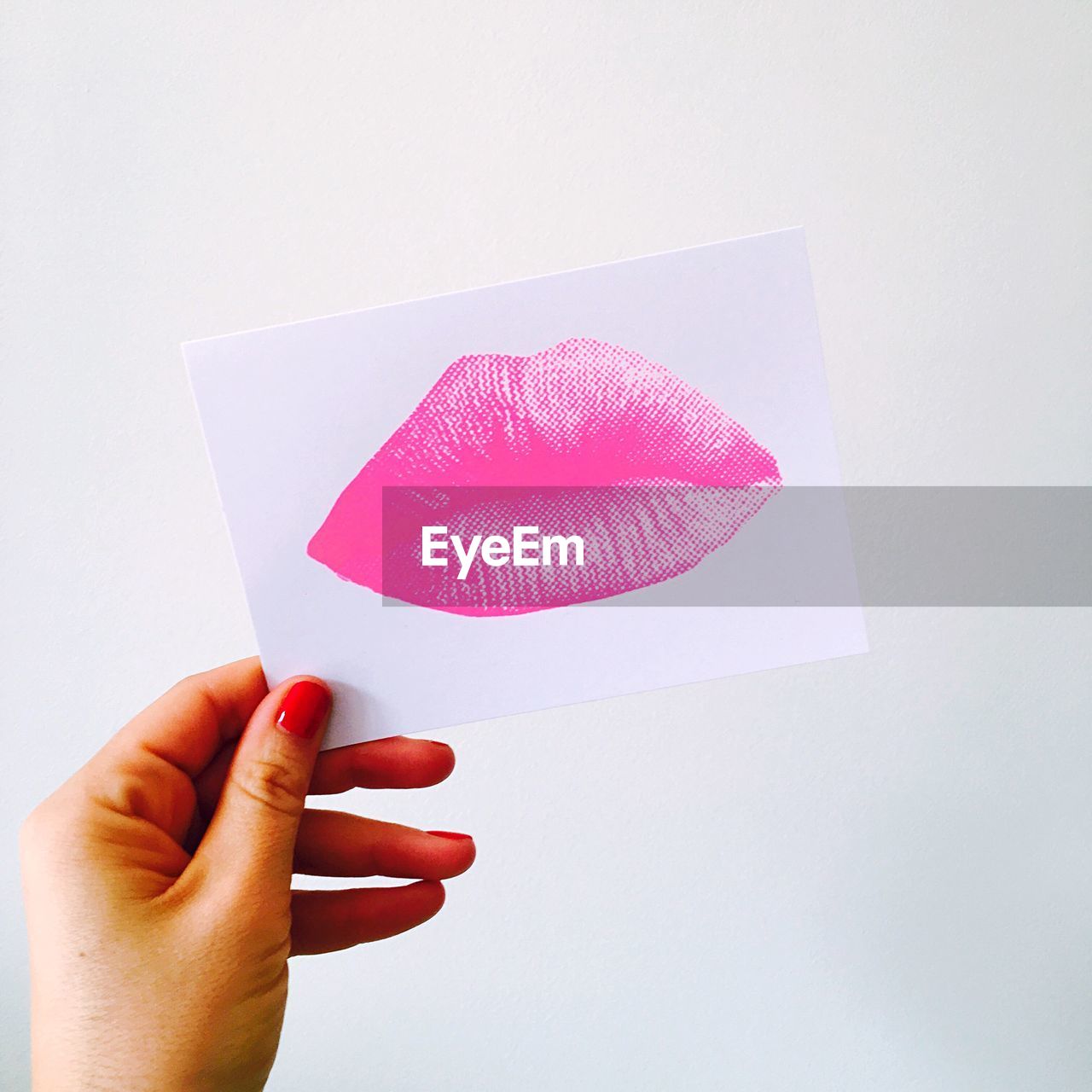 Close-up of hand holding paper with lipstick kiss against white background