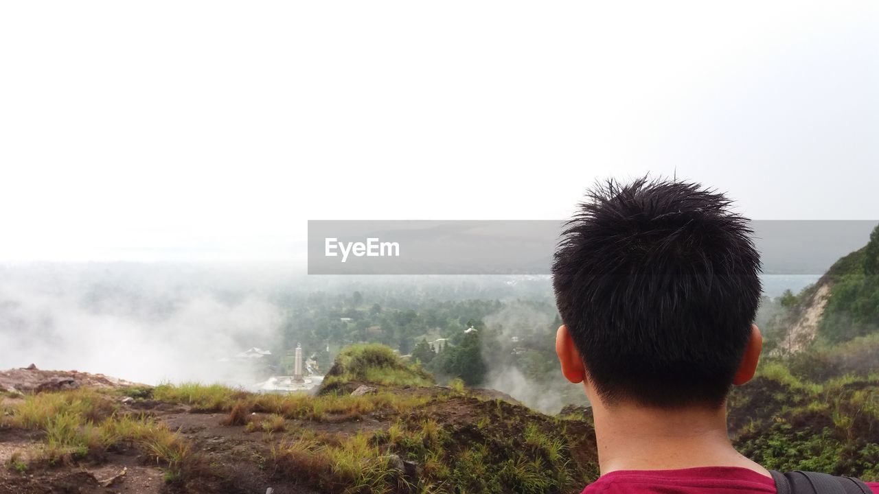 Rear view of man on mountain in foggy weather against sky
