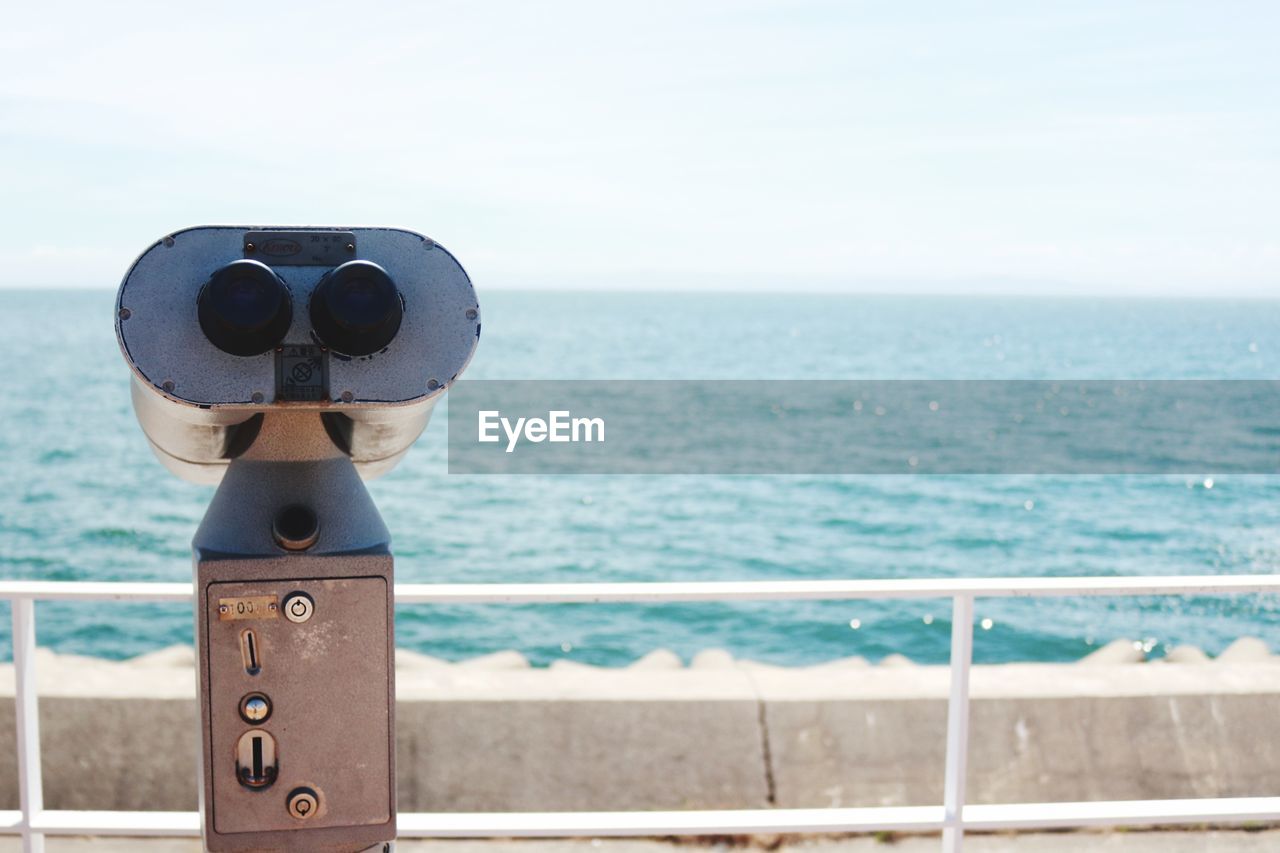 Coin-operated binoculars by sea against sky