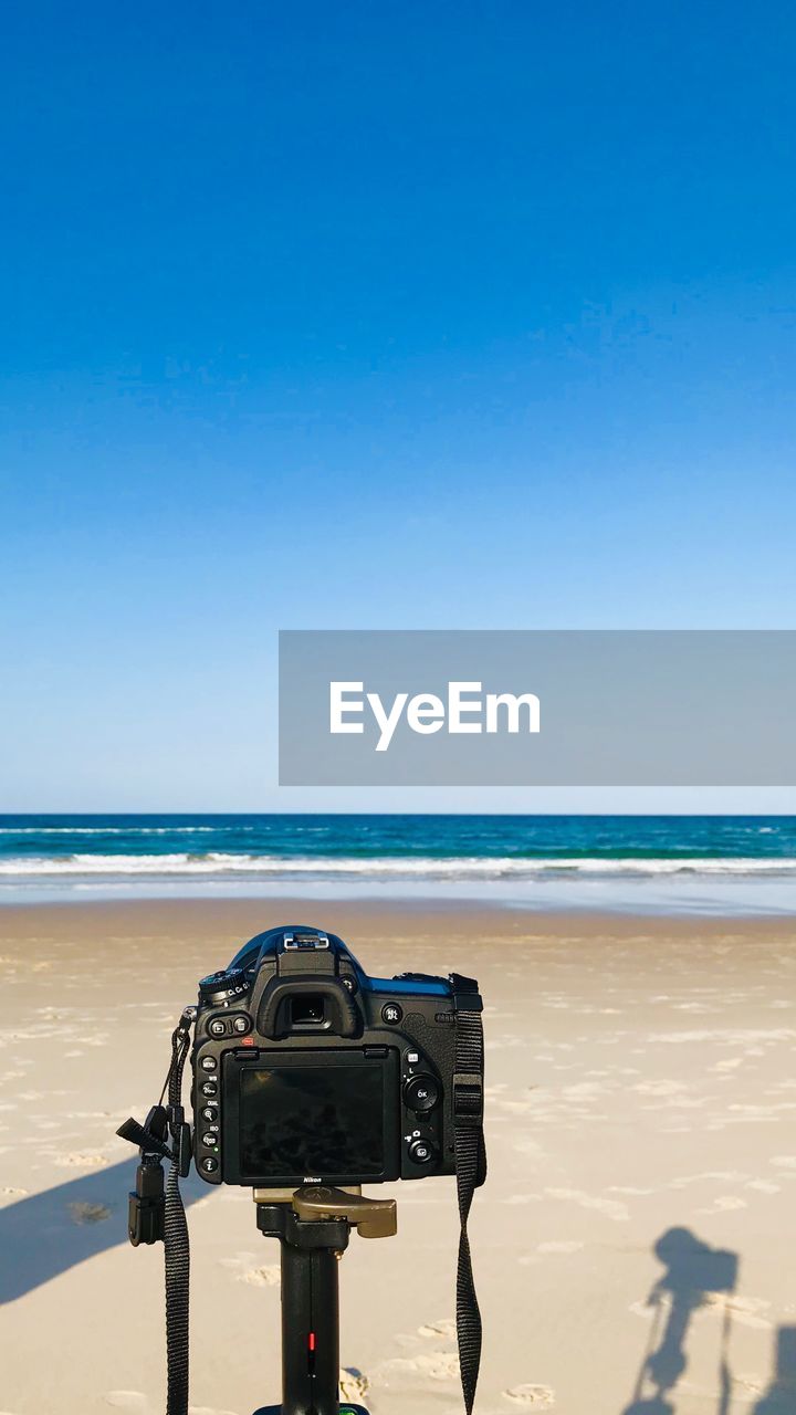 Camera on beach against clear blue sky