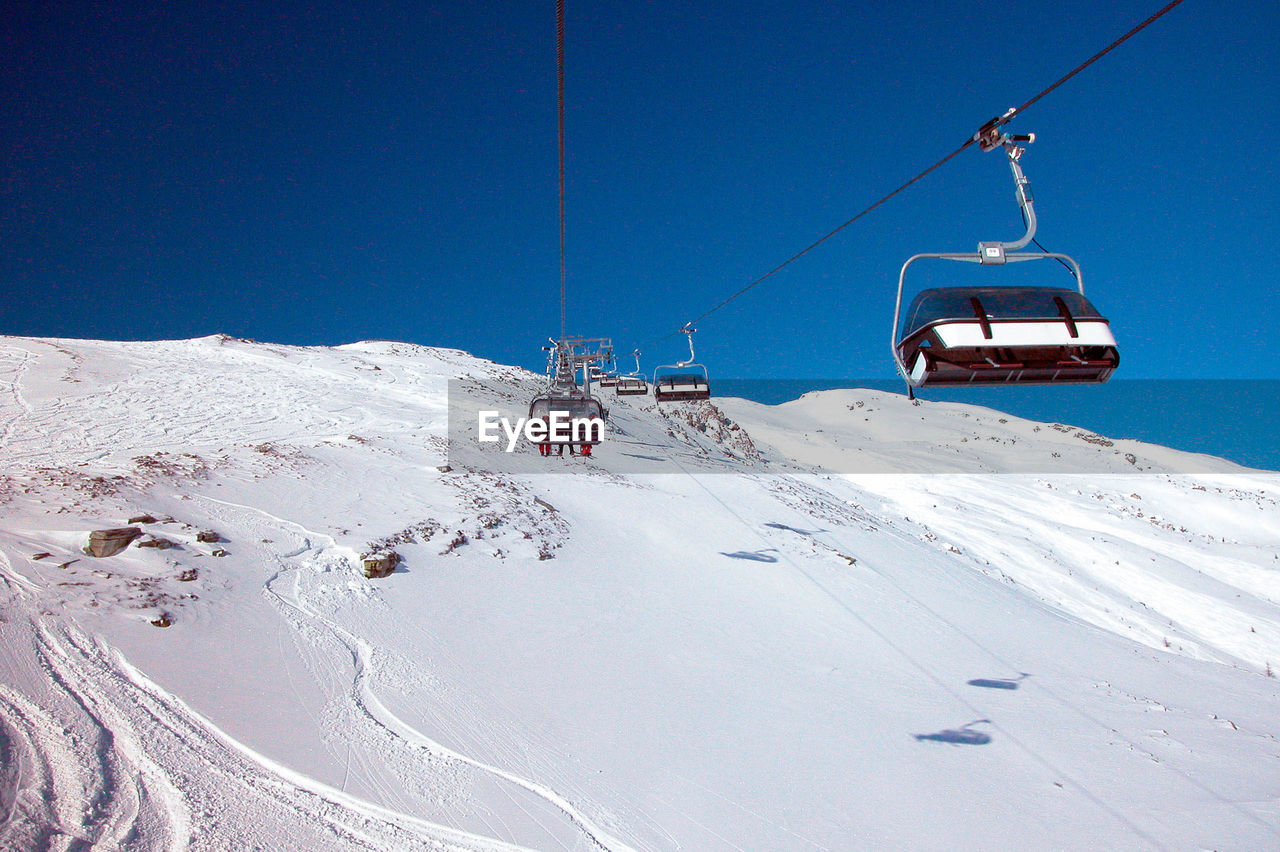 Chairlift in alpine ski area, clear blue sky, mountain slope covered in snow