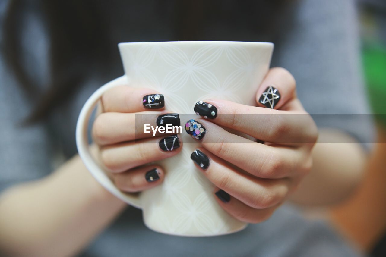 Midsection of woman with nail art holding cup