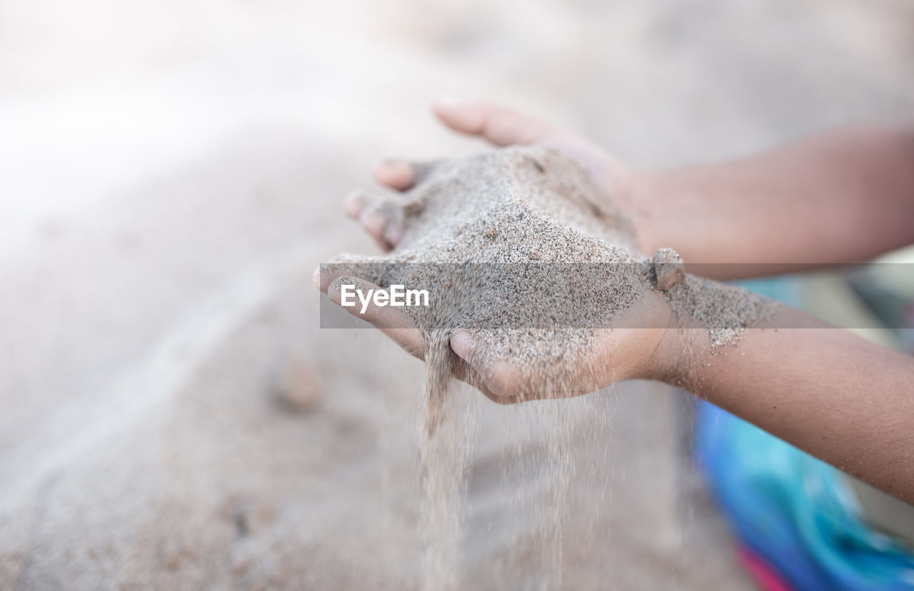 Sand puffs through the fingers of a girl's hand.