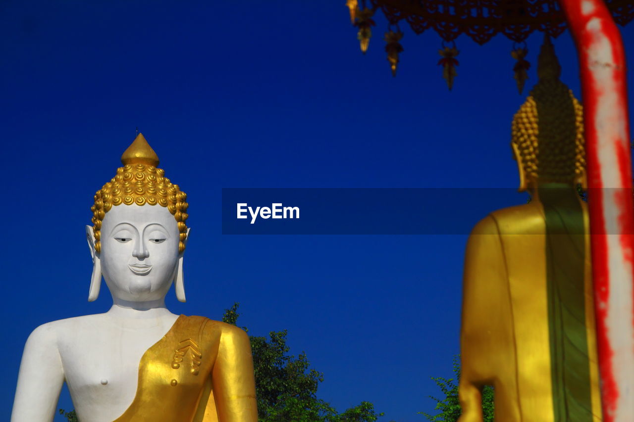 Low angle view of statue against temple against clear blue sky