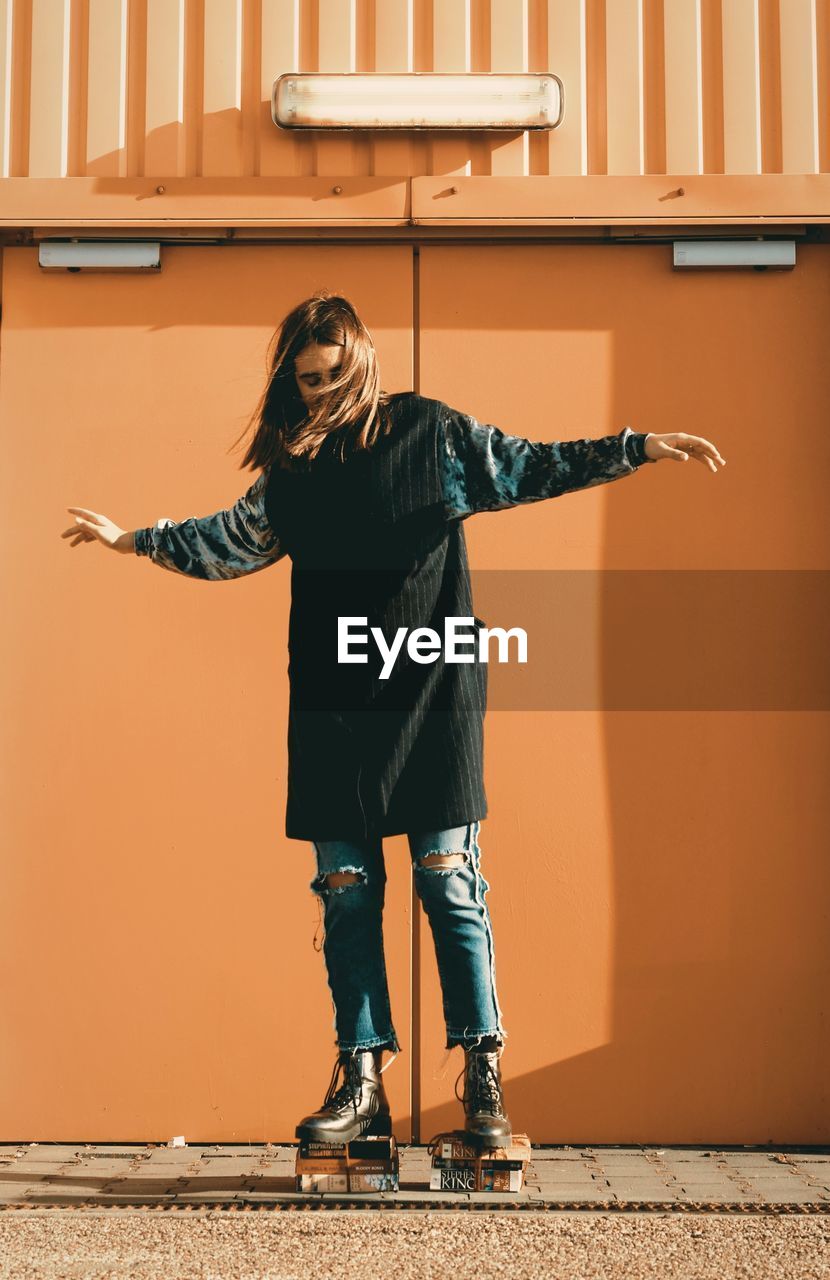 Woman standing on stacked books against orange wall