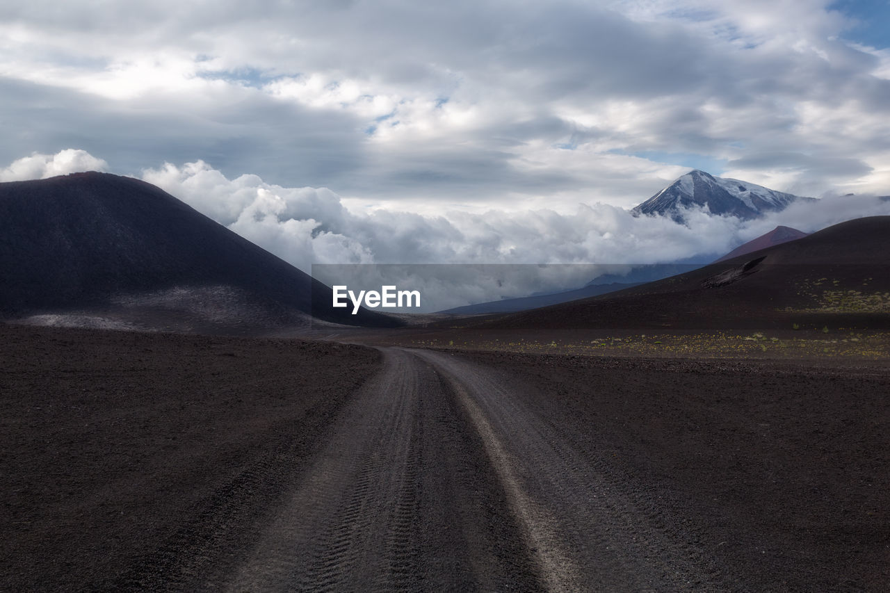 Dirt road amidst landscape and mountains against sky