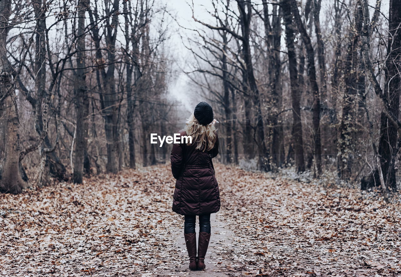 Rear view of mid adult woman standing in forest during winter