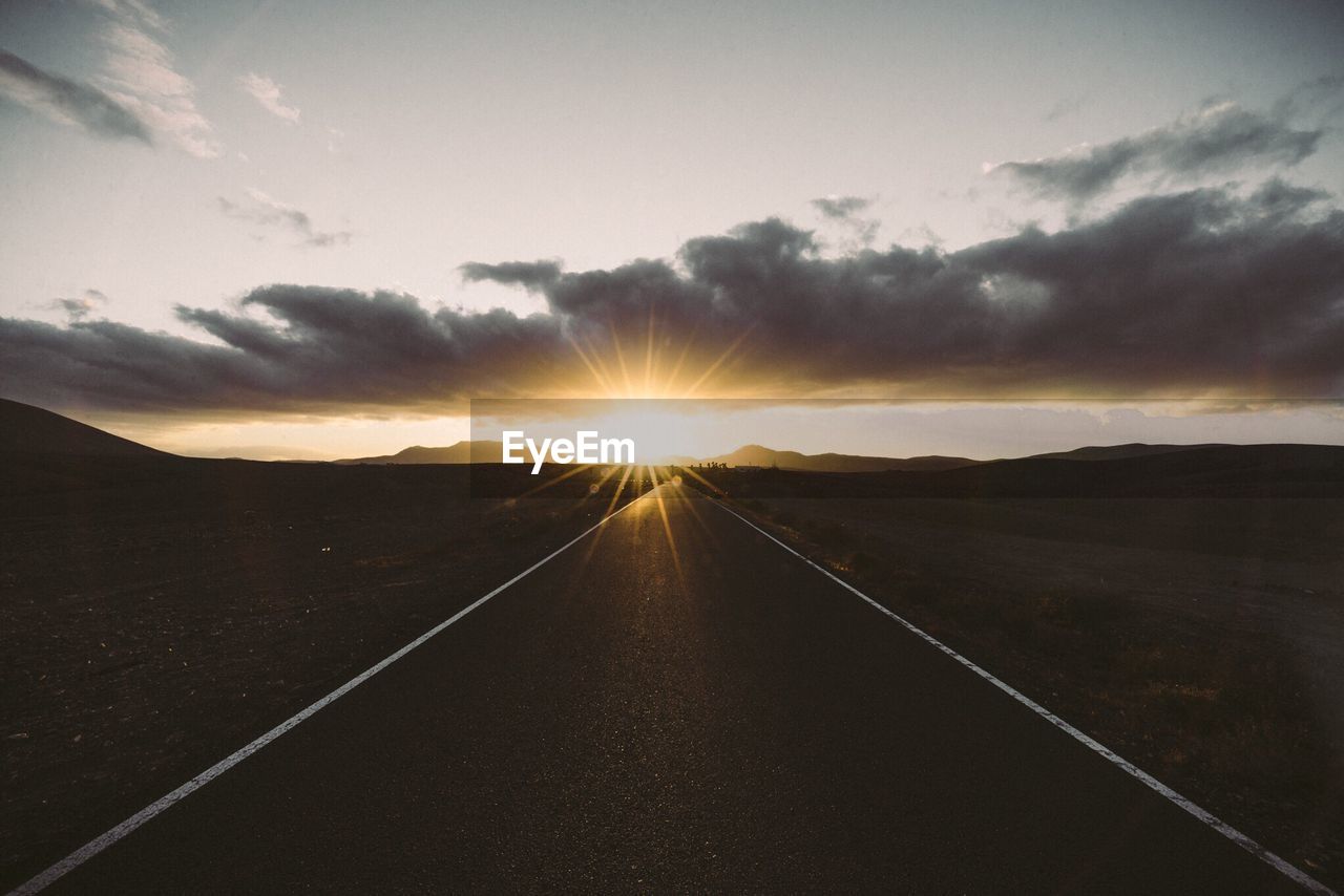 Empty road against cloudy sky during sunset