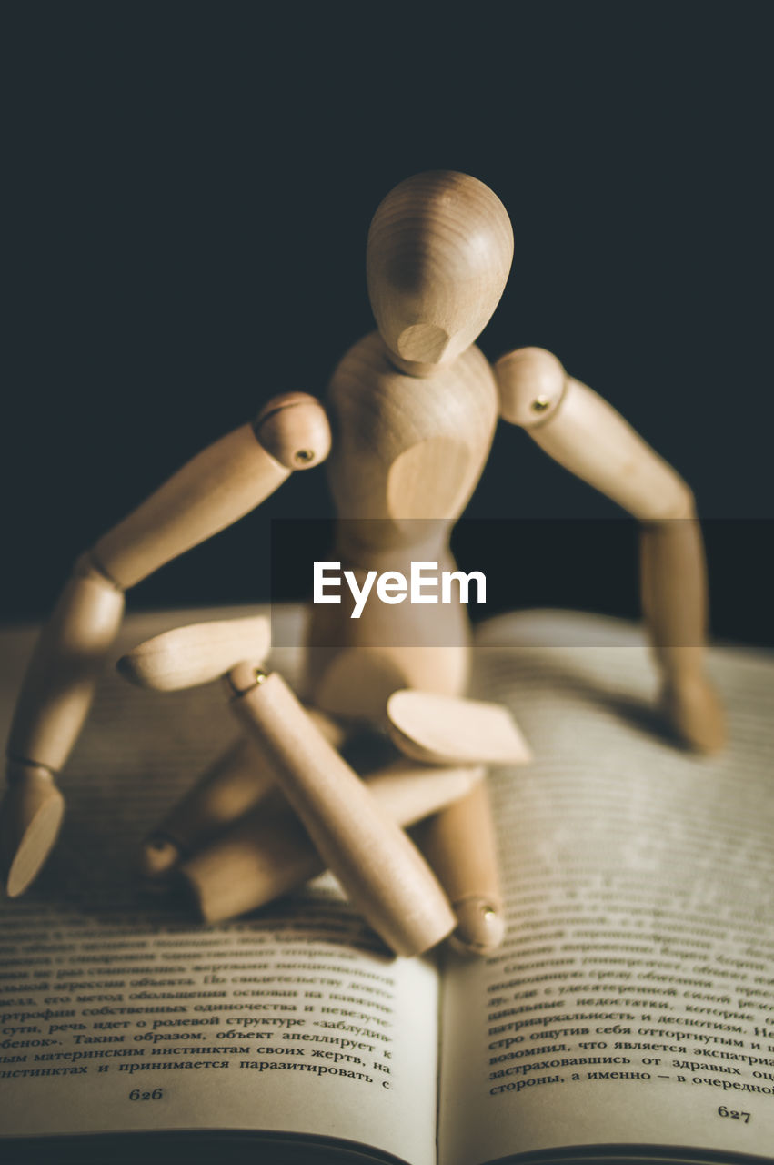 Close-up of wooden figurine sitting on book against black background