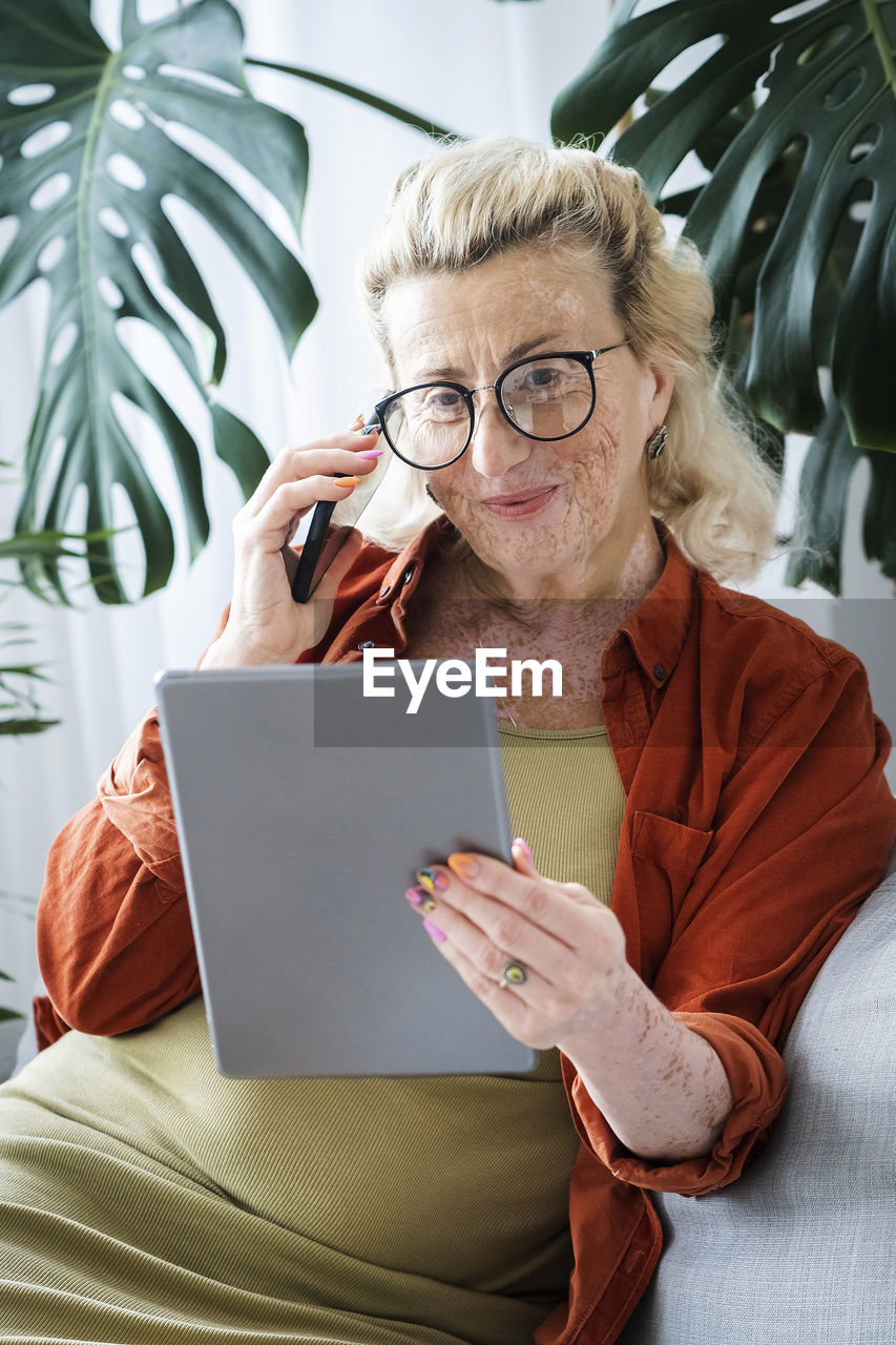 Smiling woman with vitiligo skin using wireless technologies sitting at home