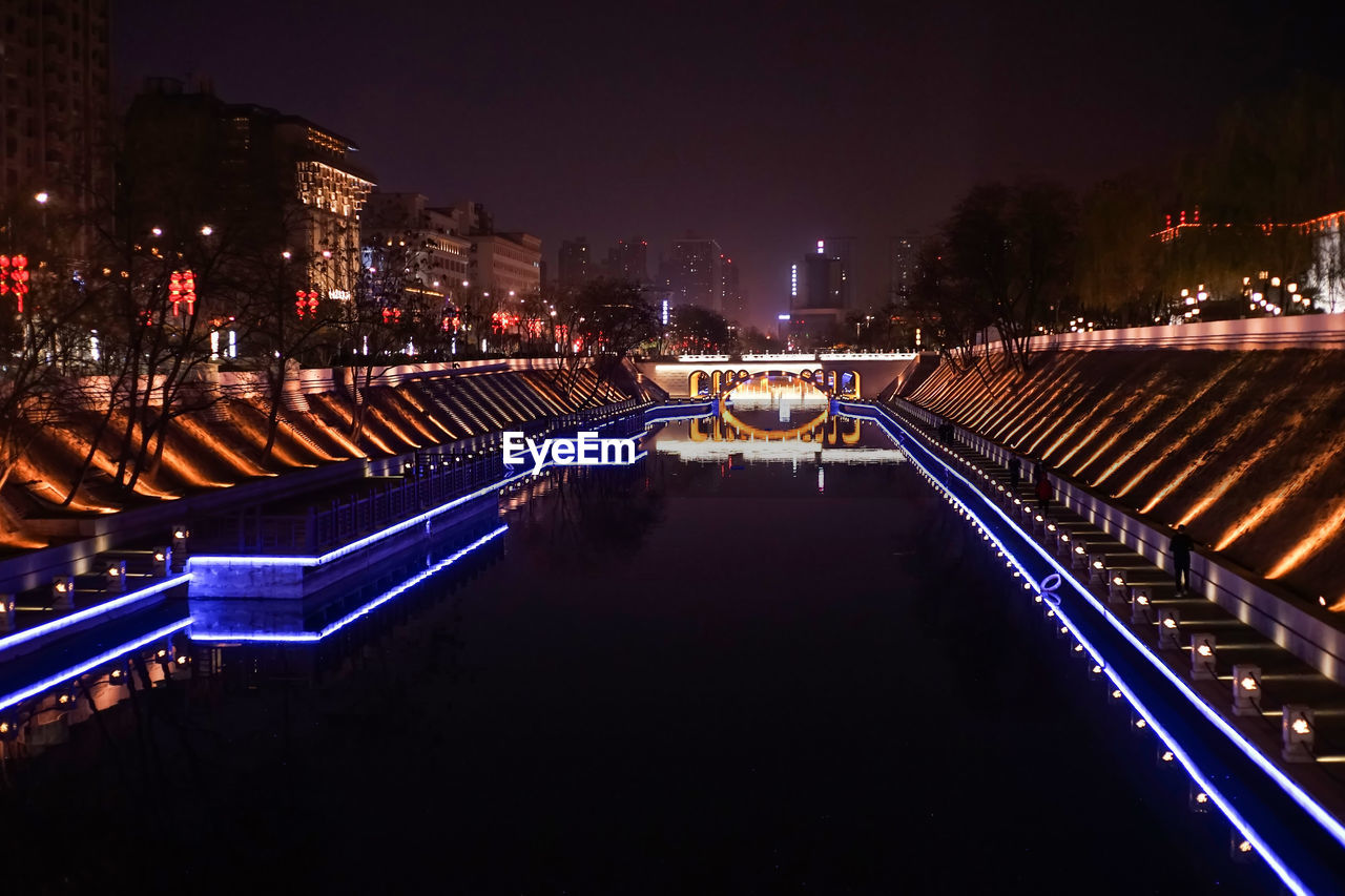 Illuminated bridge over river amidst buildings in city at night