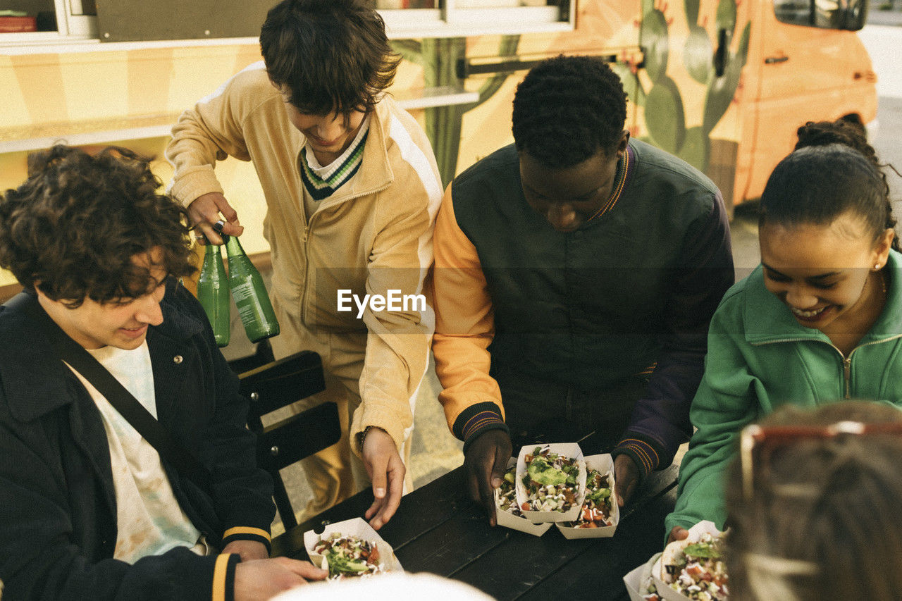 High angle view of happy friends arranging food boxes on table