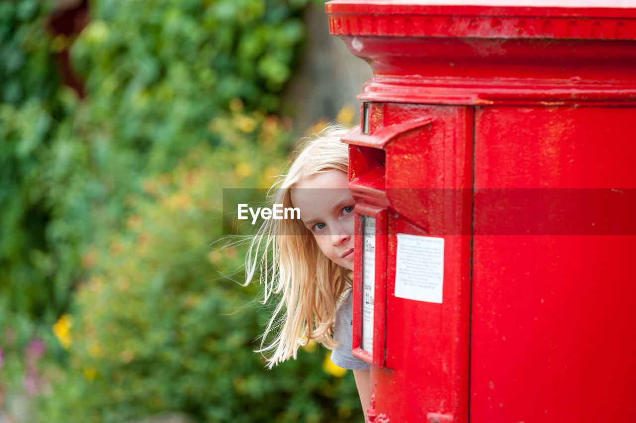 Portrait of girl peeking behind red mailbox