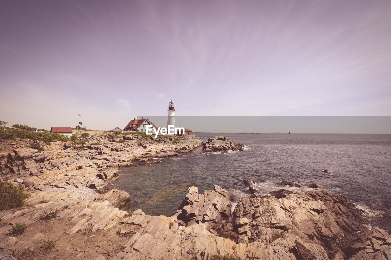 Lighthouse by sea and buildings against sky