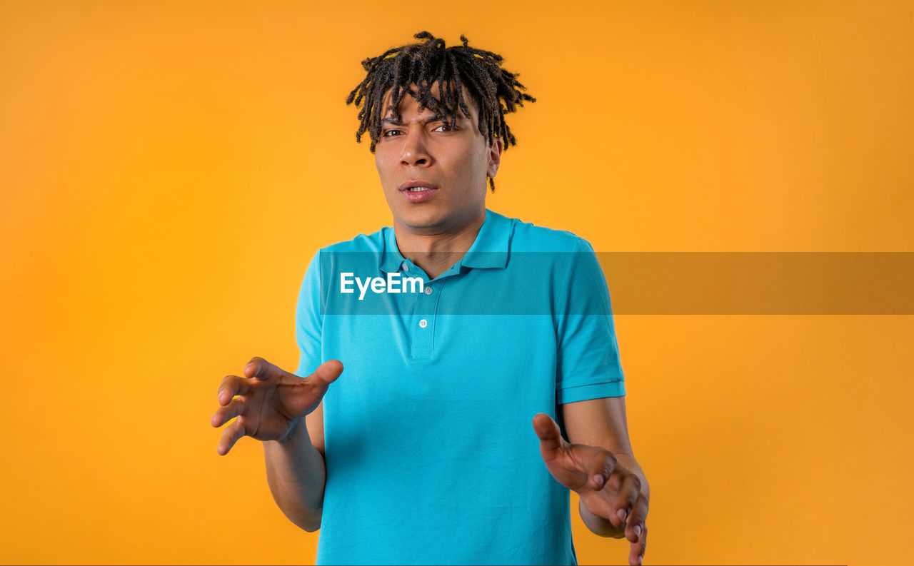 one person, colored background, adult, waist up, studio shot, yellow, men, indoors, standing, copy space, orange color, person, front view, portrait, casual clothing, yellow background, holding, young adult, lifestyles, emotion, clothing, technology, looking, polo shirt, orange background, blue