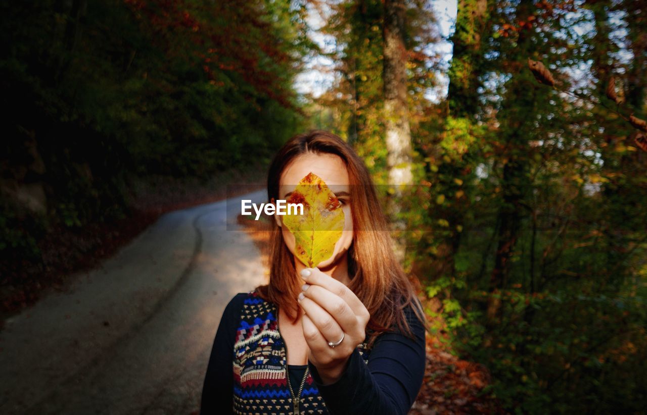 Woman holding autumn leaf against trees in forest