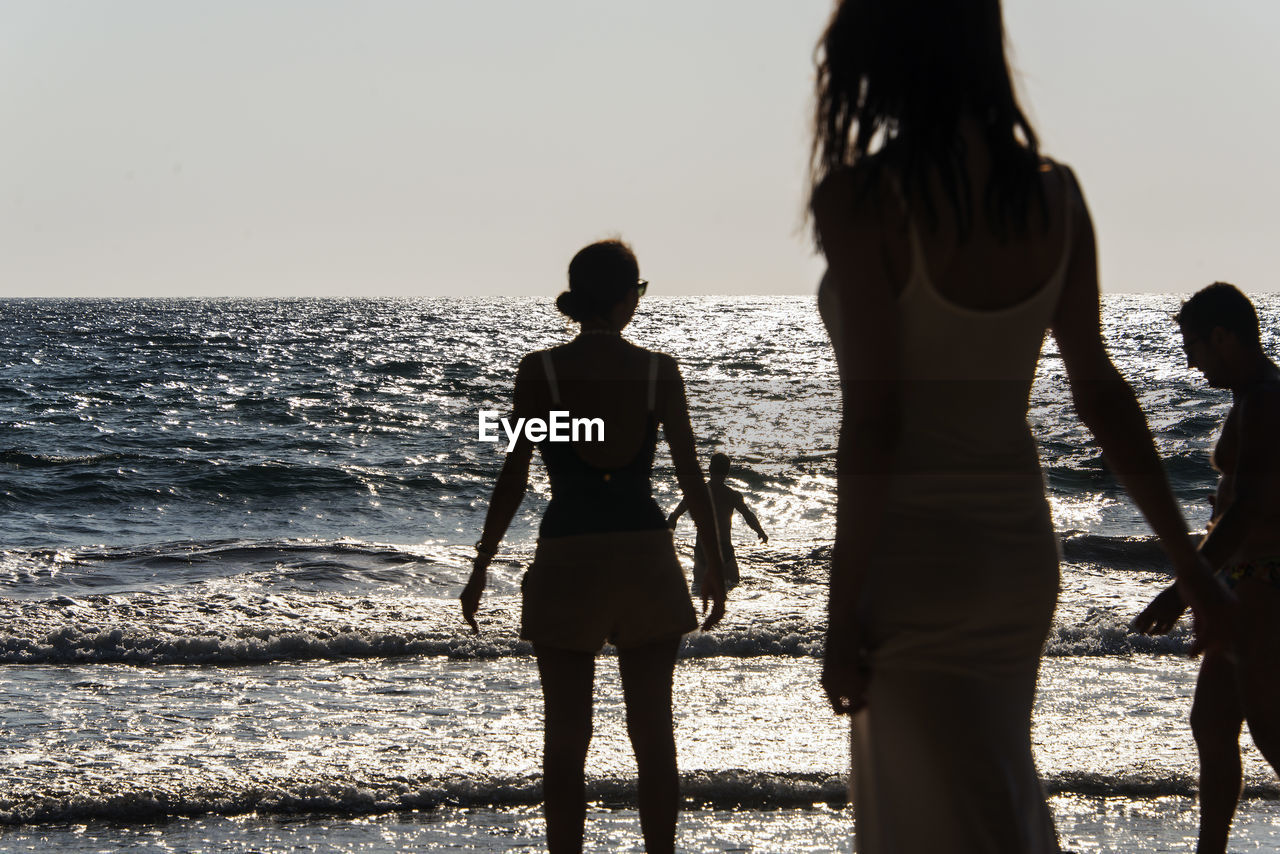 REAR VIEW OF WOMEN STANDING AT BEACH