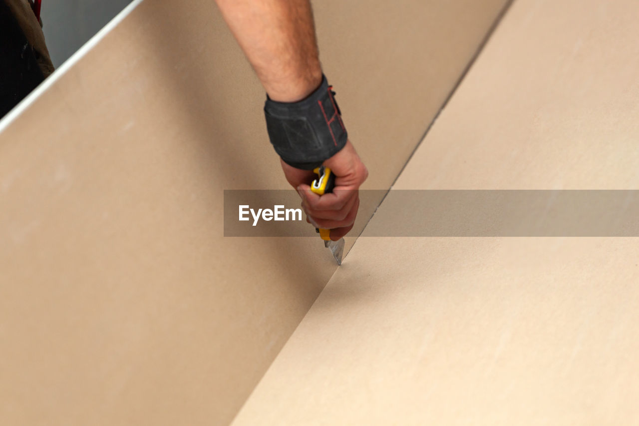 Cropped hand cutting plasterboard with work tool
