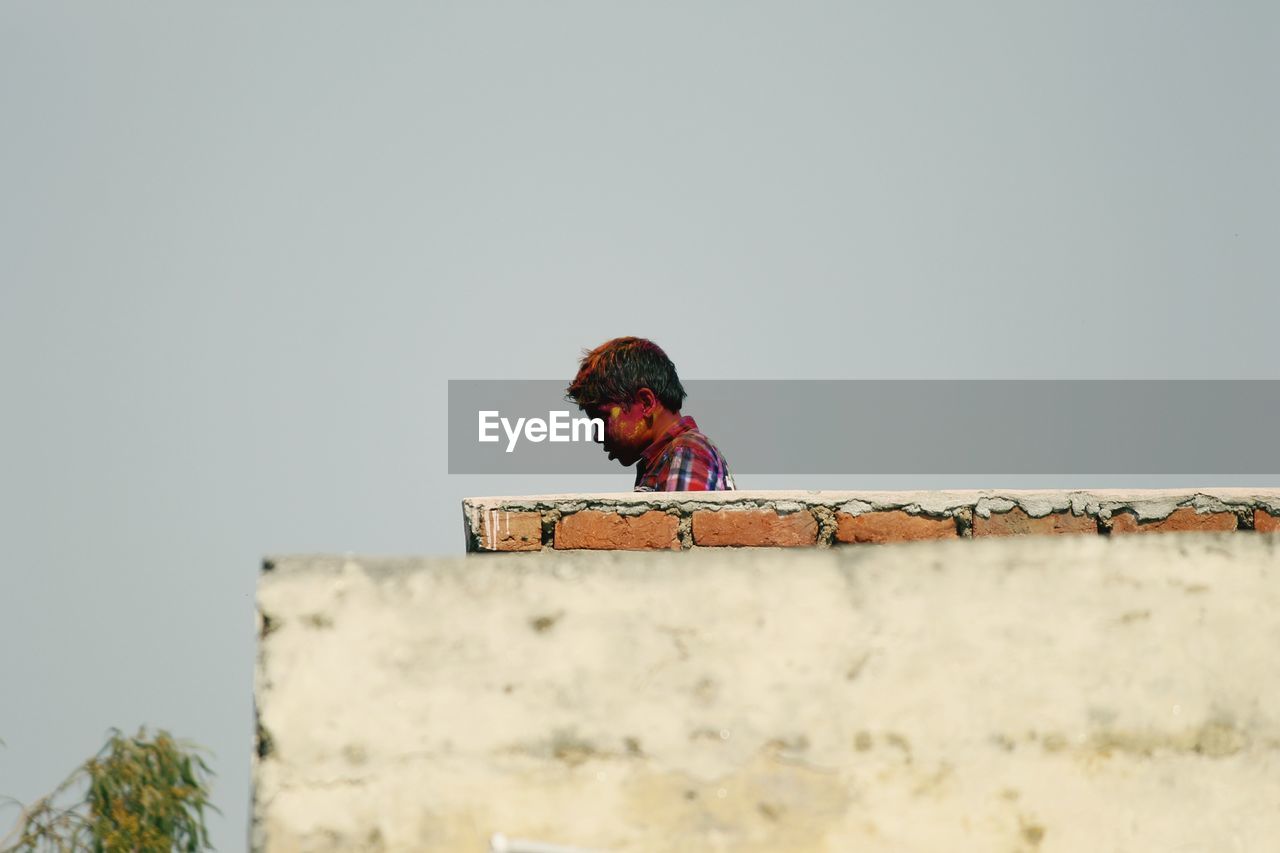 Side view of boy with powder paint against clear sky during holi festival