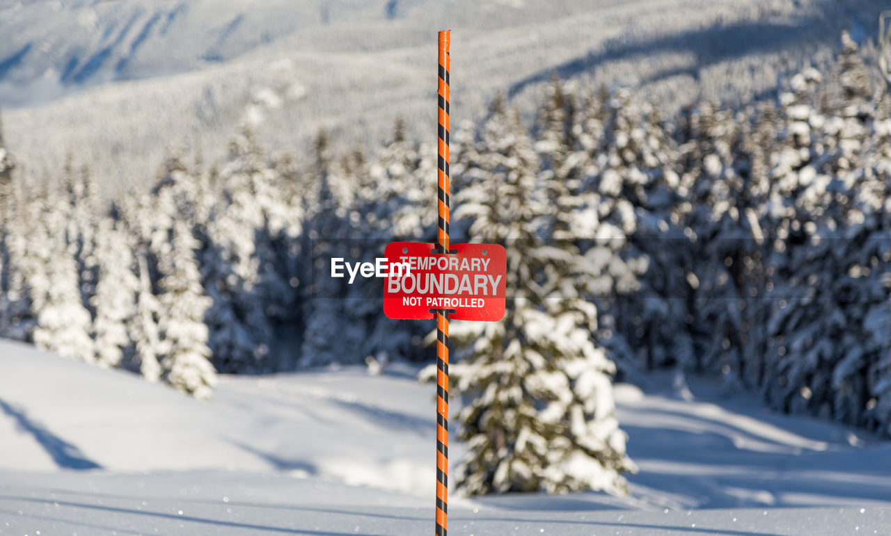 INFORMATION SIGN ON SNOW COVERED ROAD AGAINST MOUNTAIN