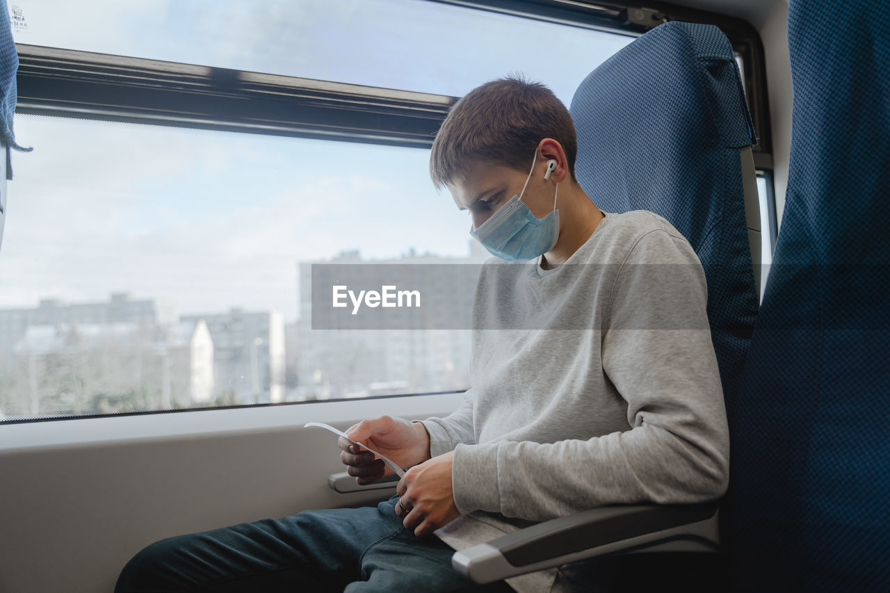 Young man wearing mask sitting by train window