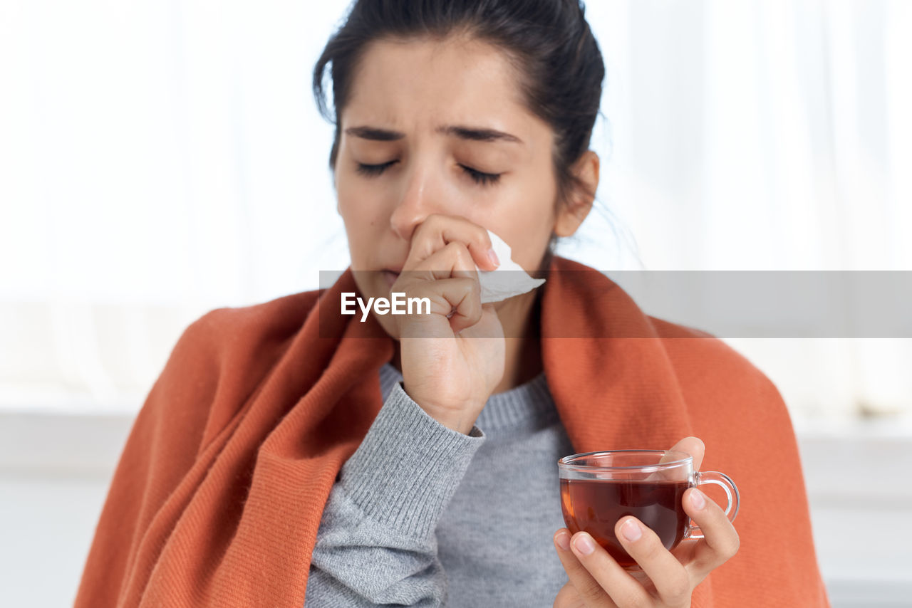 Sick woman wiping nose while holding tea