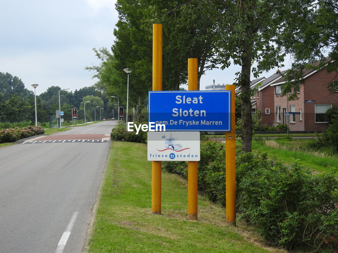 Road sign by trees against sky