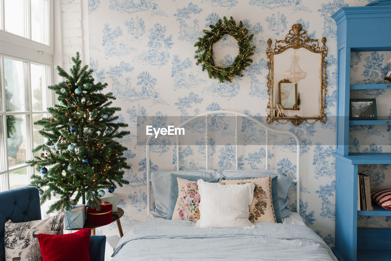 Pillows on the bed, a christmas wreath on the wall, a christmas tree by the window