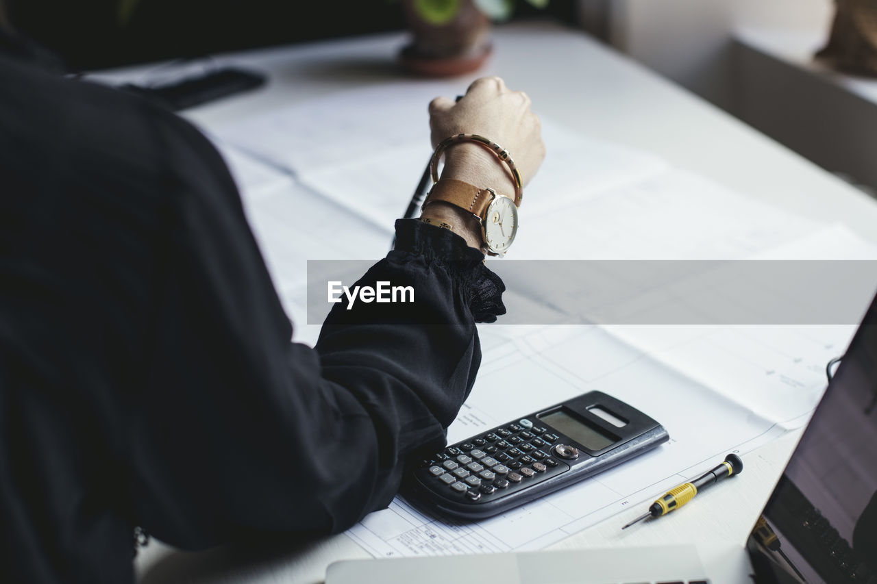 Cropped image of female engineer with blueprint and calculator on desk