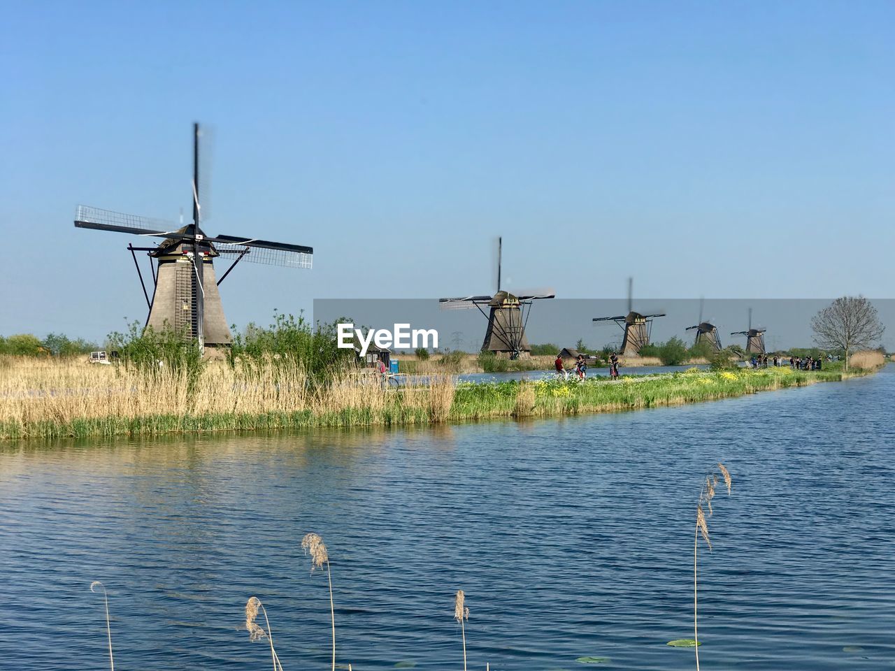 WINDMILLS BY LAKE AGAINST CLEAR BLUE SKY