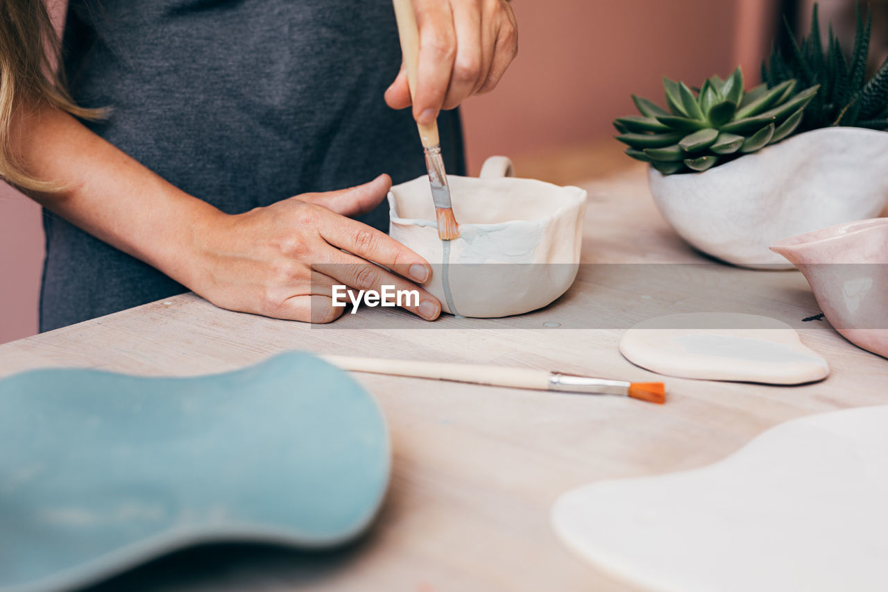 Midsection of woman painting pitcher at desk