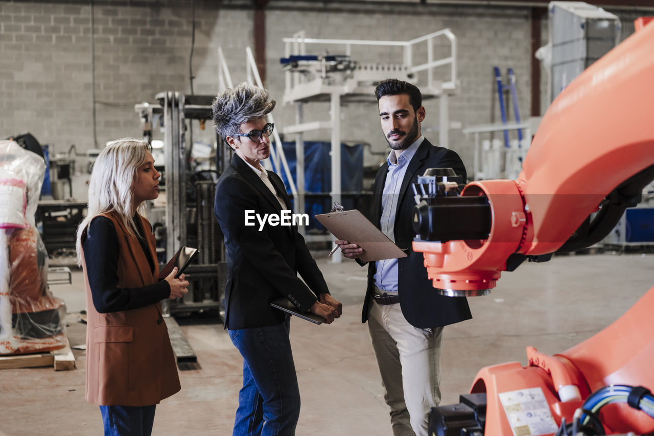 Engineers discussing over robotic arm in industry