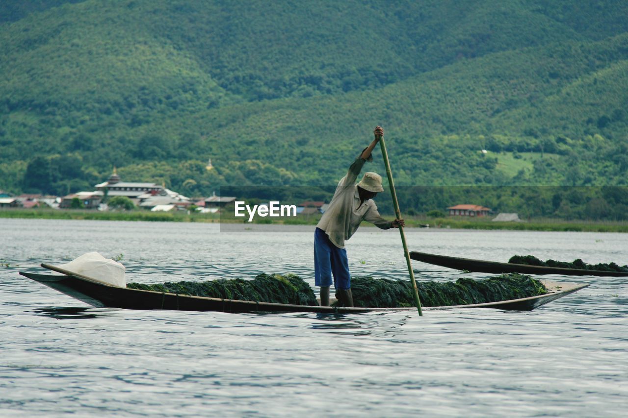 MAN IN BOAT SAILING ON RIVER AGAINST MOUNTAIN