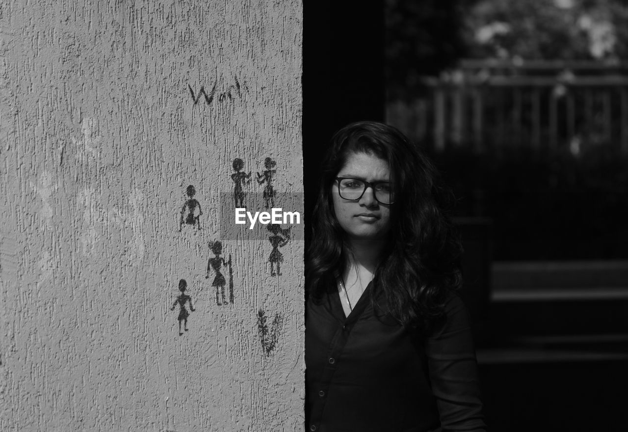 Portrait of young woman standing by wall