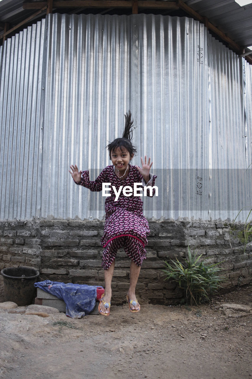 Portrait of girl jumping against corrugated iron