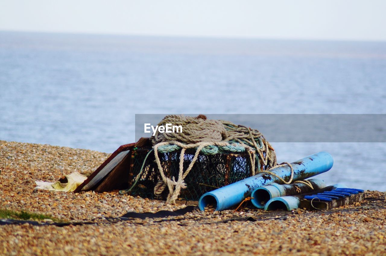 Fishing net with rope and pipes at beach against sky