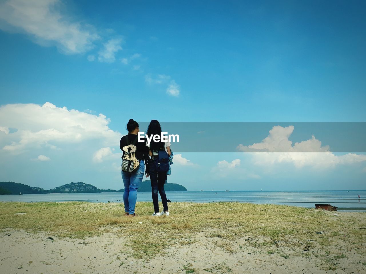 Rear view of women standing at beach against sky