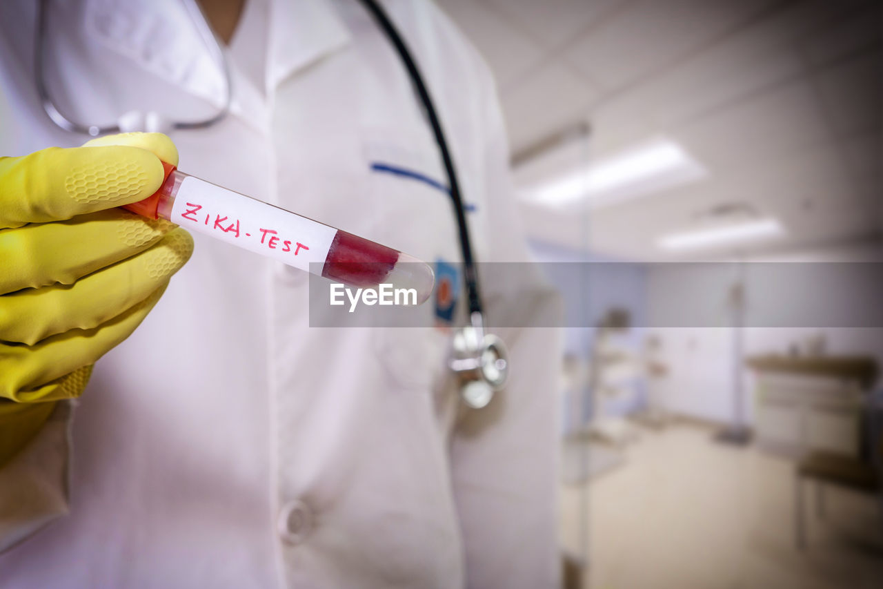 Midsection of doctor holding test tube with text in hospital