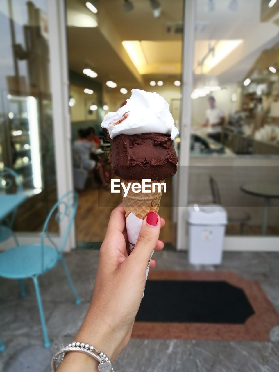 CROPPED HAND HOLDING ICE CREAM CONE AGAINST BLURRED BACKGROUND