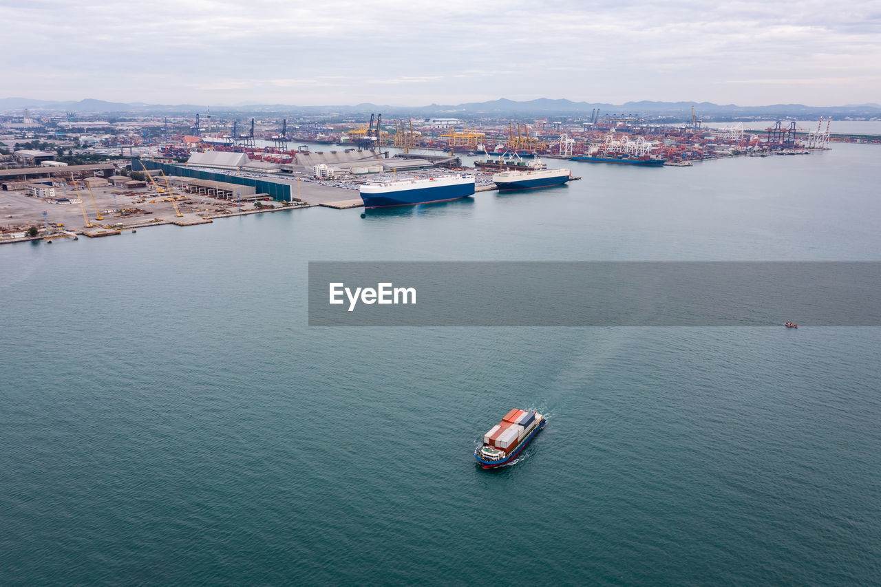 Small container ship sailing in sea and shipping port background photograph aerial view from drone