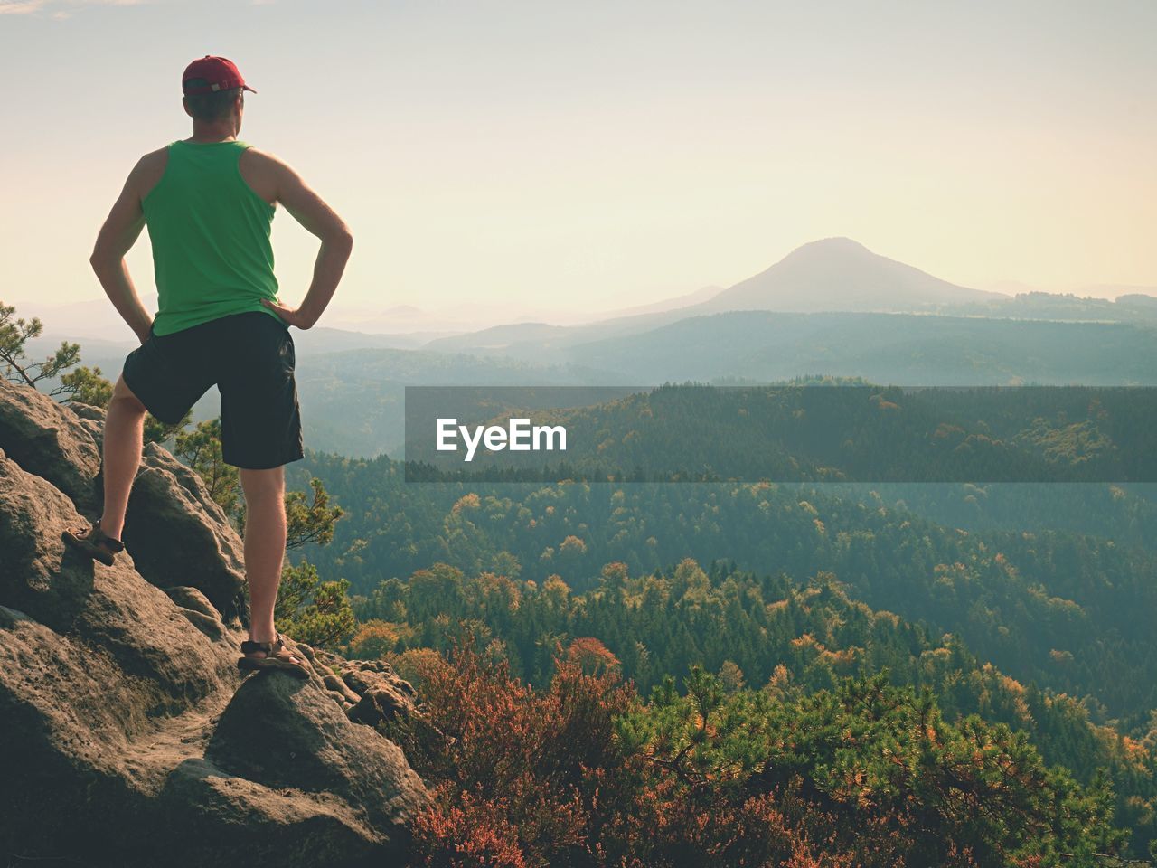 MAN STANDING ON ROCKS LOOKING AT MOUNTAINS