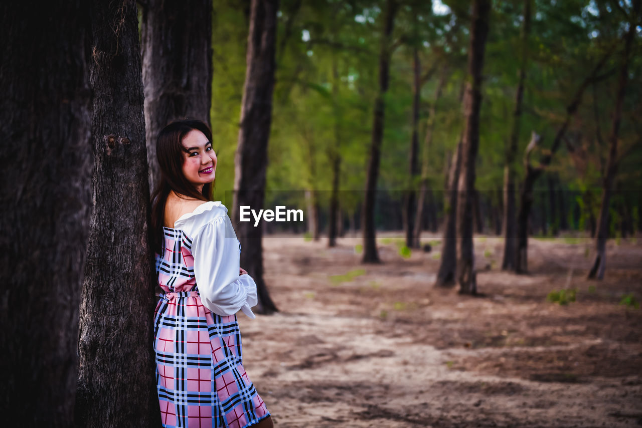 SMILING YOUNG WOMAN STANDING ON TREE TRUNK IN FOREST