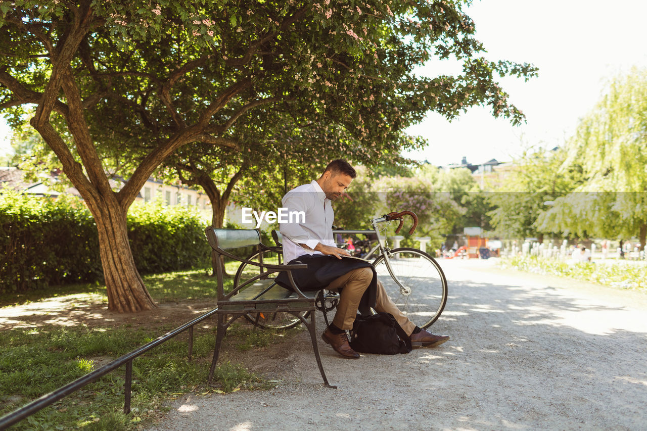 Businessman using laptop while sitting on bench at park